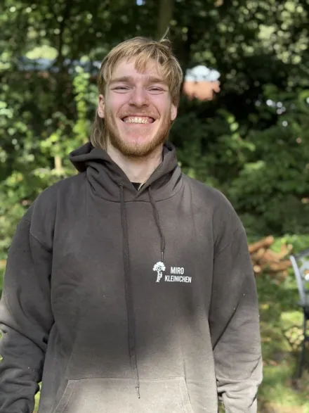 Marlin Schiller im Firmenpullover vor Bäumen